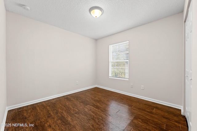 spare room featuring baseboards, dark wood-type flooring, and a textured ceiling