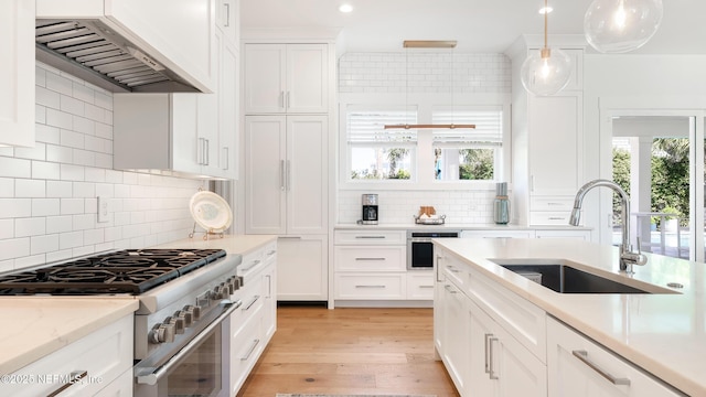 kitchen featuring light wood-style flooring, custom range hood, a sink, high end stainless steel range oven, and white cabinets