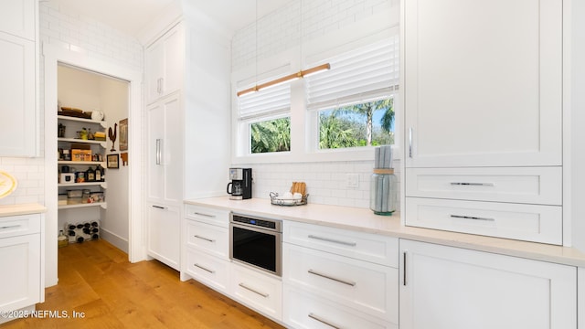 kitchen featuring light wood-type flooring, backsplash, white cabinets, light countertops, and stainless steel oven