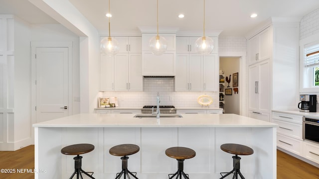 kitchen with tasteful backsplash, stainless steel oven, white cabinets, and a sink