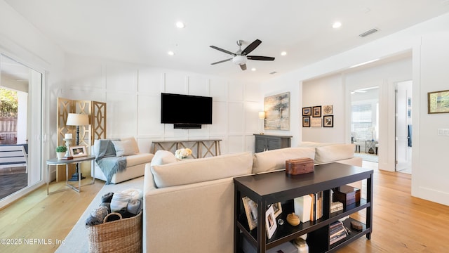 living area featuring a decorative wall, light wood-style flooring, a ceiling fan, and visible vents