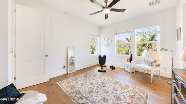 sitting room with light wood-type flooring, visible vents, baseboards, and ceiling fan