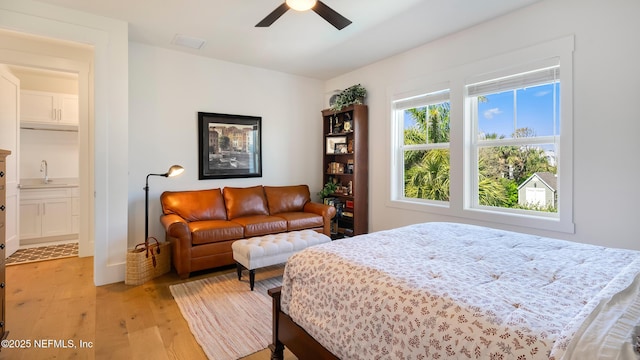 bedroom featuring visible vents, light wood-style flooring, a ceiling fan, and a sink