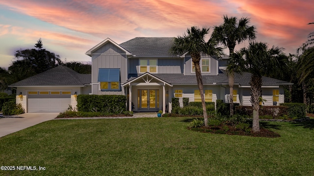 view of front facade featuring a lawn, french doors, an attached garage, and driveway