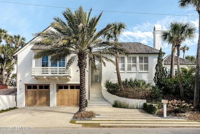 view of front of house featuring a chimney, stucco siding, concrete driveway, stairway, and a garage