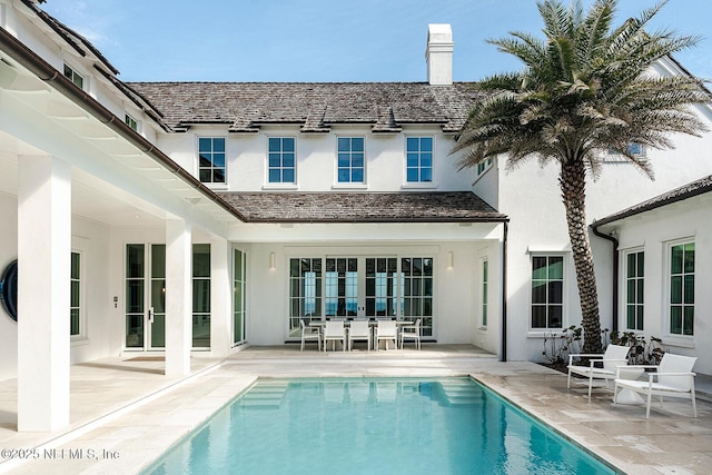 back of house with an outdoor pool, a patio, a chimney, and stucco siding