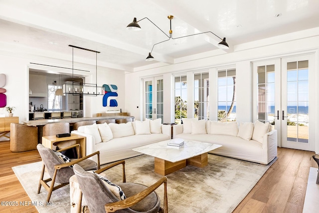 living room featuring a chandelier, french doors, beamed ceiling, and light wood-type flooring