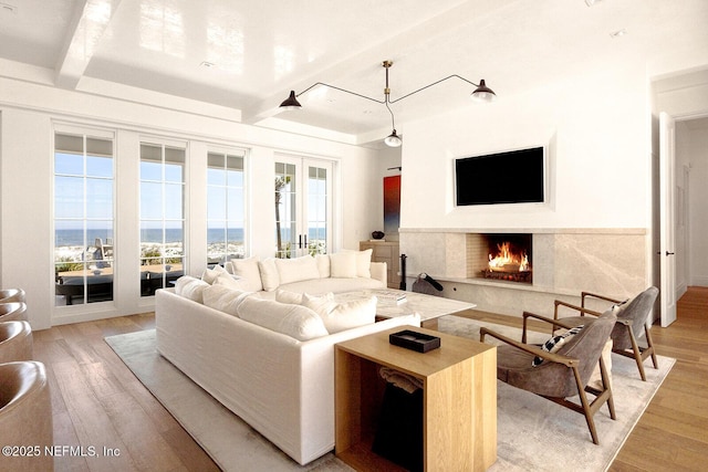 living room featuring a high end fireplace, beam ceiling, and light wood-style flooring