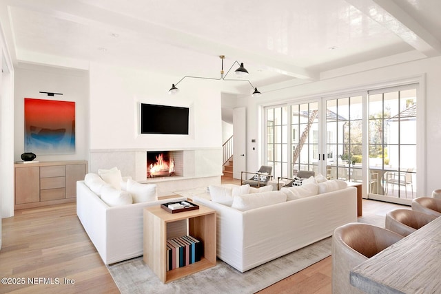 living area with french doors, light wood finished floors, stairway, a premium fireplace, and beamed ceiling