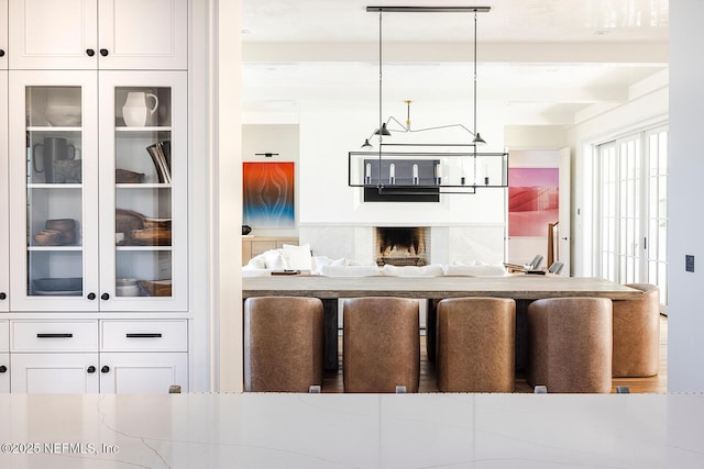 kitchen featuring beamed ceiling, glass insert cabinets, white cabinetry, and decorative light fixtures