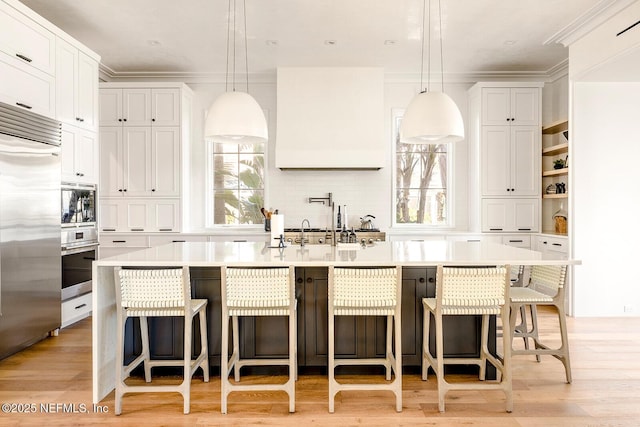 kitchen featuring built in appliances, light countertops, light wood finished floors, and a center island with sink