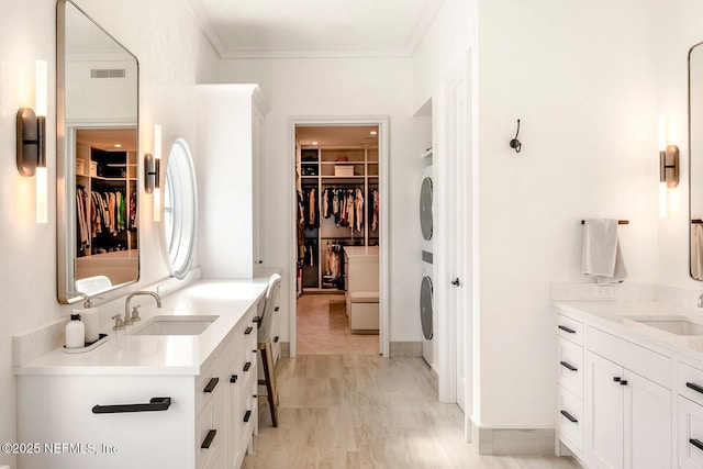 bathroom with crown molding, stacked washer and clothes dryer, visible vents, and a sink