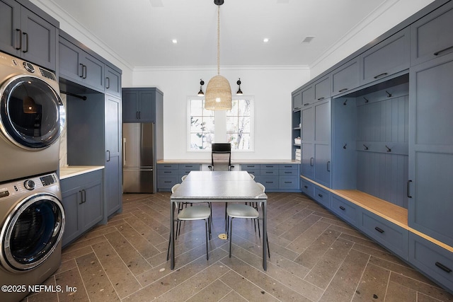 laundry area featuring cabinet space, crown molding, and stacked washer and clothes dryer