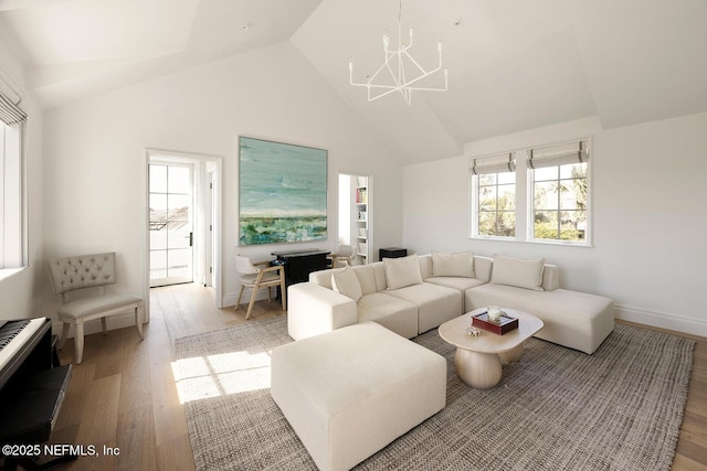 living area with baseboards, high vaulted ceiling, an inviting chandelier, and light wood-style floors