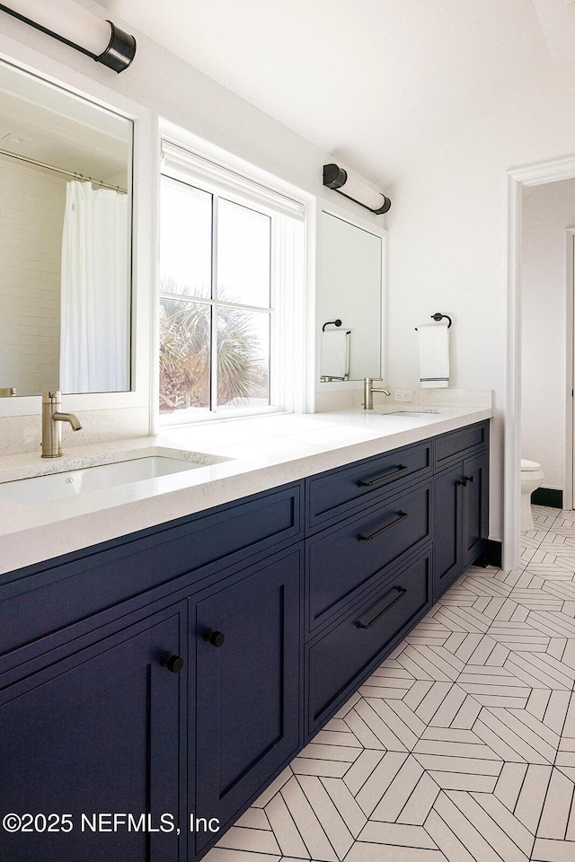 bathroom with double vanity, a sink, and toilet