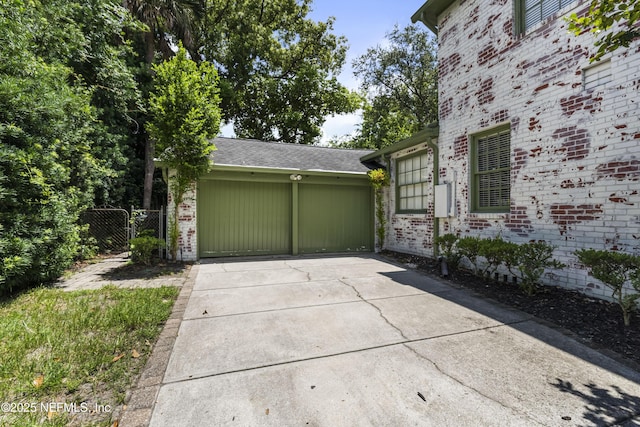 view of side of property with a garage, brick siding, fence, driveway, and a gate