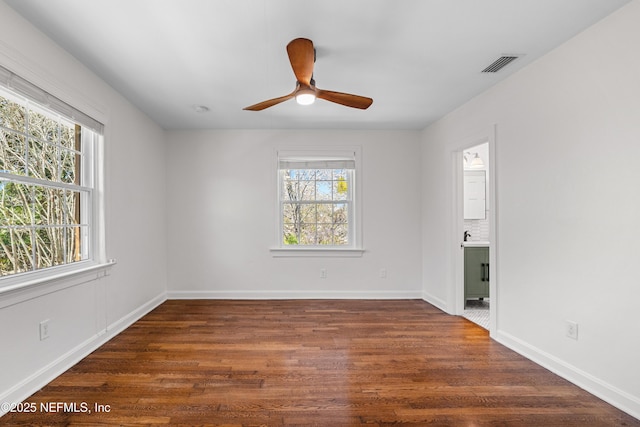 spare room featuring a wealth of natural light, dark wood-style flooring, visible vents, and baseboards