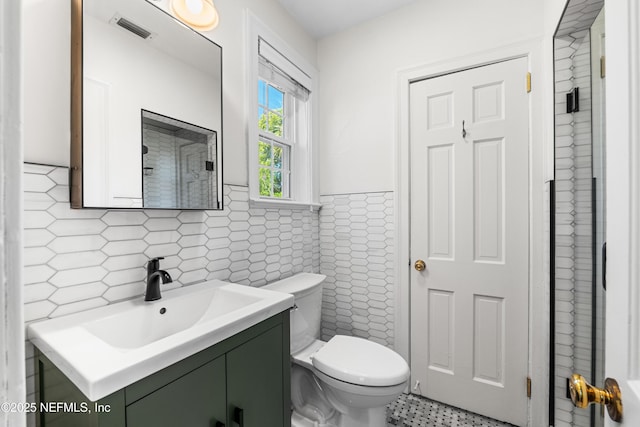 bathroom with visible vents, wainscoting, toilet, vanity, and tile walls