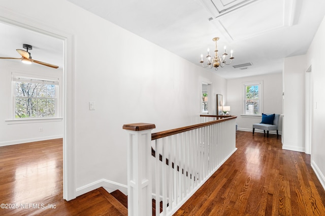 hall featuring baseboards, a chandelier, wood finished floors, and an upstairs landing