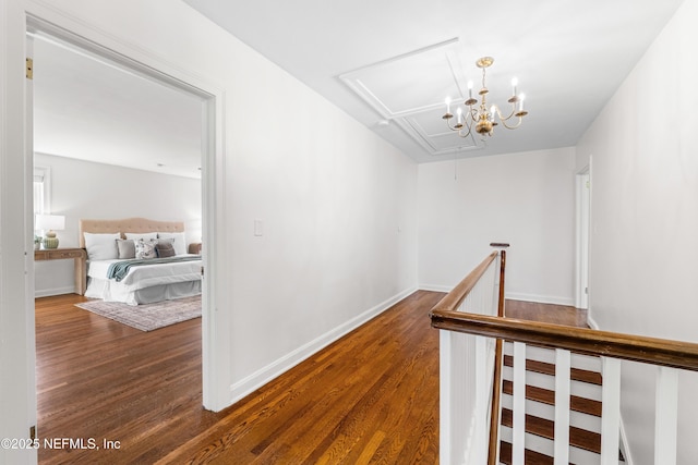 corridor featuring wood finished floors, an upstairs landing, baseboards, attic access, and an inviting chandelier