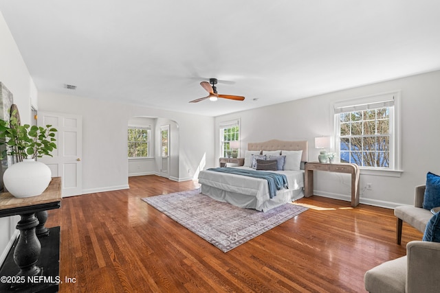 bedroom featuring arched walkways, visible vents, a ceiling fan, wood finished floors, and baseboards