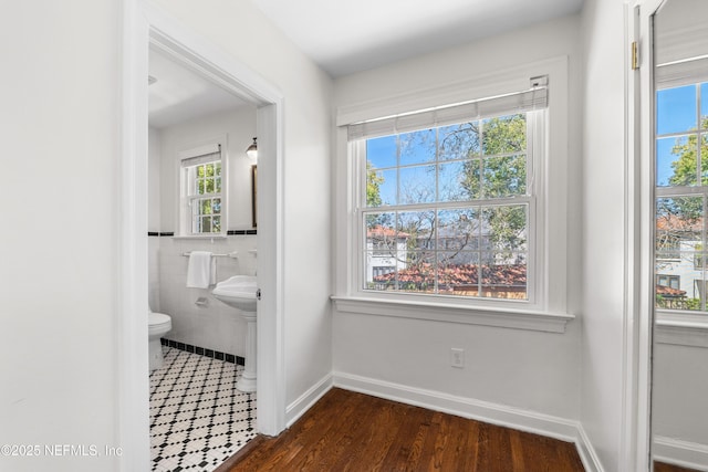 bathroom featuring baseboards, wood finished floors, toilet, and tile walls