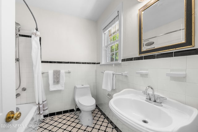 bathroom featuring toilet, a sink, tile walls, wainscoting, and shower / bath combo