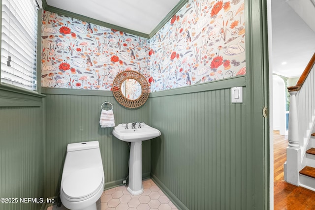 bathroom featuring a wainscoted wall, crown molding, toilet, a sink, and wallpapered walls