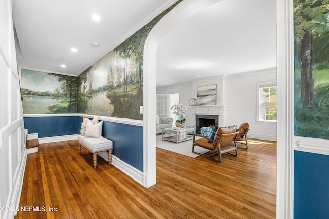 sitting room featuring arched walkways, a fireplace, ornamental molding, wood finished floors, and baseboards