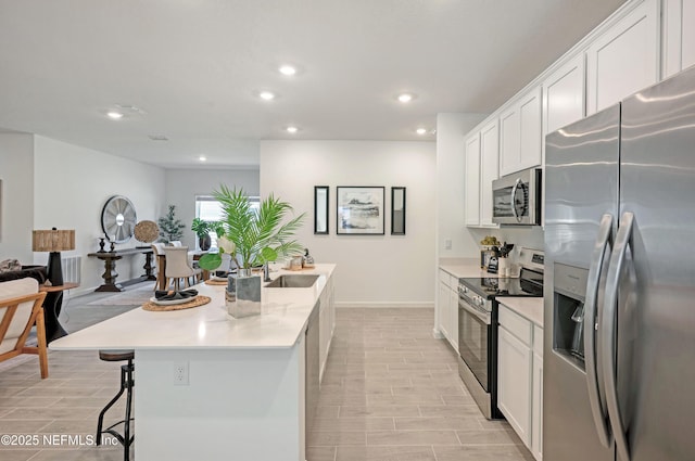 kitchen featuring a breakfast bar area, recessed lighting, stainless steel appliances, white cabinetry, and a kitchen island with sink