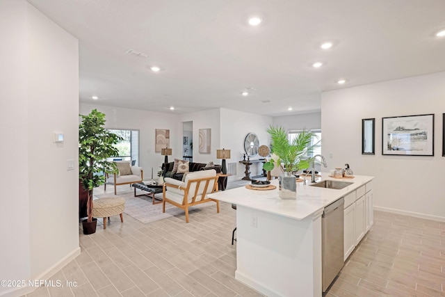 kitchen featuring a kitchen island with sink, a sink, light countertops, white cabinets, and stainless steel dishwasher