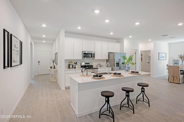 kitchen featuring white cabinetry, wood tiled floor, a kitchen island with sink, stainless steel appliances, and a kitchen bar