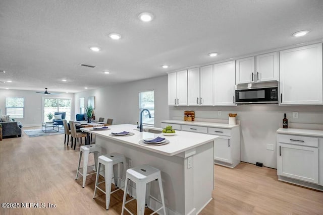 kitchen featuring light wood finished floors, visible vents, stainless steel microwave, open floor plan, and a sink