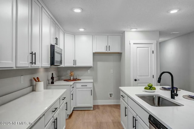 kitchen featuring white cabinetry, stainless steel microwave, light countertops, and a sink