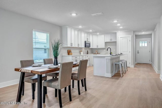 kitchen with a healthy amount of sunlight, light wood-style flooring, a kitchen island with sink, and baseboards