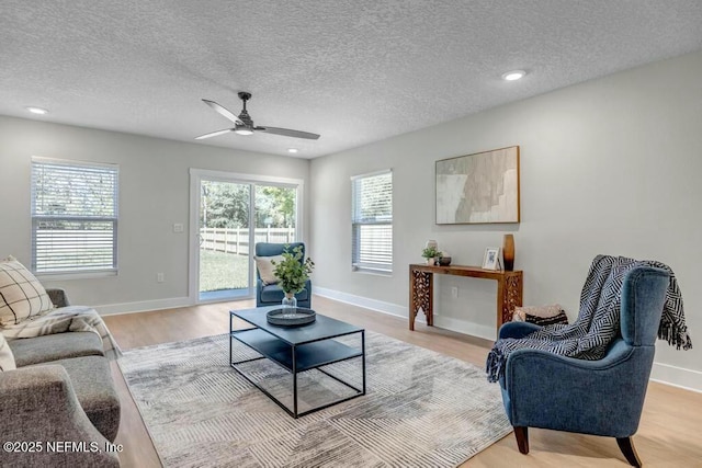 living room featuring recessed lighting, light wood-style flooring, baseboards, and a textured ceiling