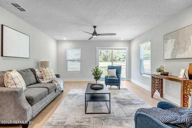 living area featuring light wood-type flooring, plenty of natural light, visible vents, and baseboards