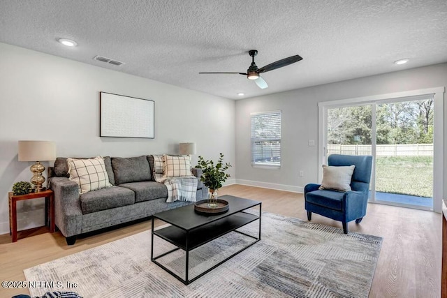 living area featuring light wood-style floors, baseboards, visible vents, and a textured ceiling