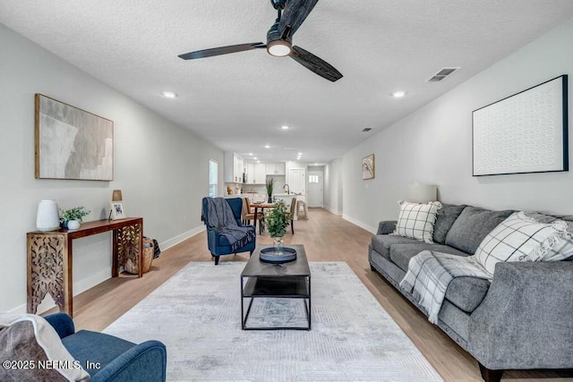 living room with light wood-style floors, baseboards, visible vents, and a textured ceiling