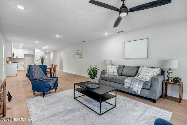 living area featuring baseboards, light wood-style flooring, visible vents, and a textured ceiling