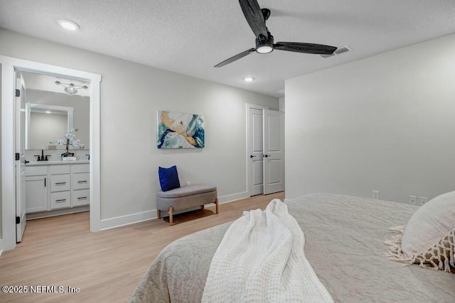 bedroom with visible vents, light wood-style flooring, a sink, a textured ceiling, and baseboards