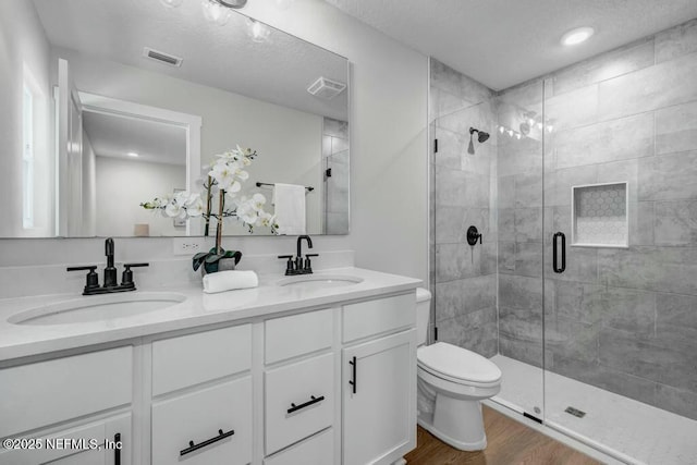 full bathroom featuring a stall shower, visible vents, a sink, and wood finished floors