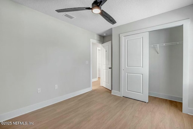 unfurnished bedroom with a closet, visible vents, a textured ceiling, wood finished floors, and baseboards