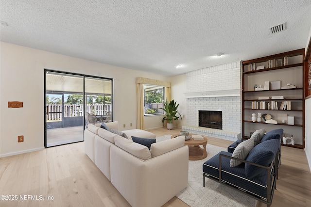 living area with visible vents, light wood-style floors, a fireplace, and a textured ceiling