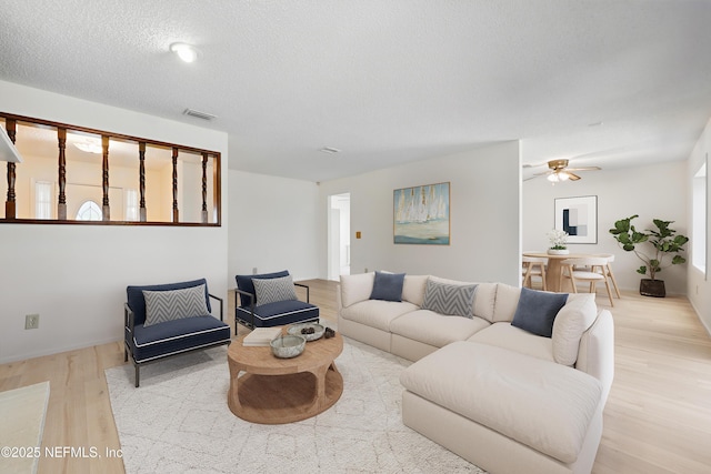 living room featuring ceiling fan, wood finished floors, visible vents, and a textured ceiling