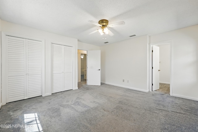 unfurnished bedroom featuring baseboards, visible vents, a textured ceiling, carpet flooring, and two closets