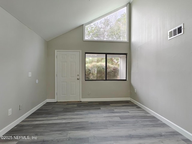 empty room featuring high vaulted ceiling, baseboards, visible vents, and wood finished floors