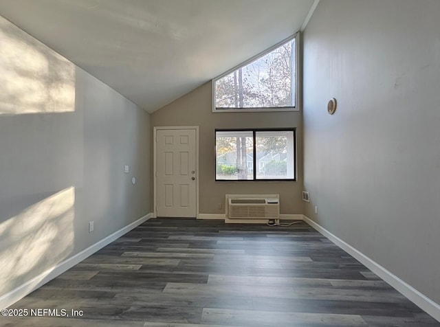 empty room with high vaulted ceiling, an AC wall unit, dark wood finished floors, and baseboards