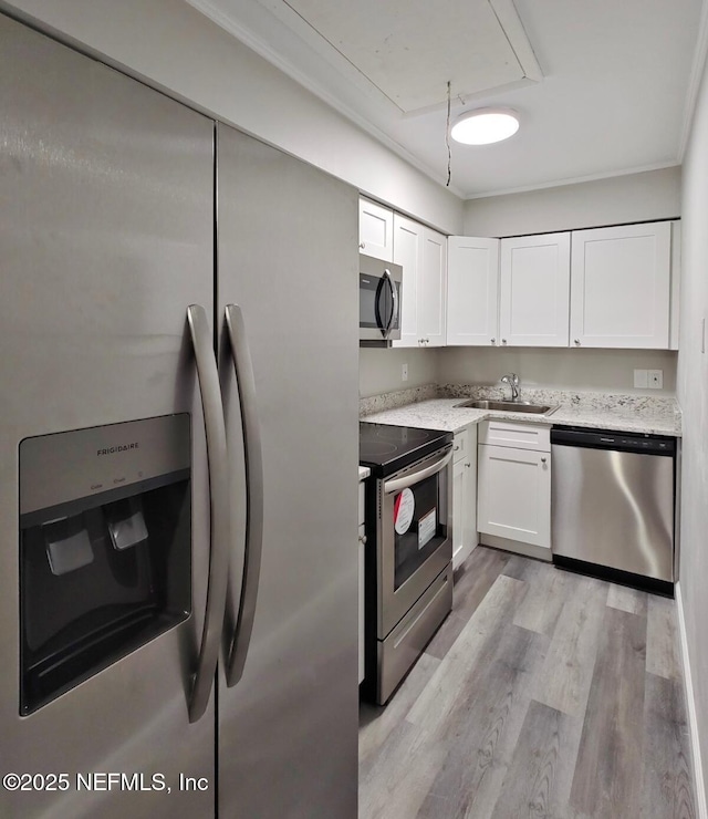 kitchen with light wood-style flooring, a sink, white cabinets, appliances with stainless steel finishes, and light stone countertops