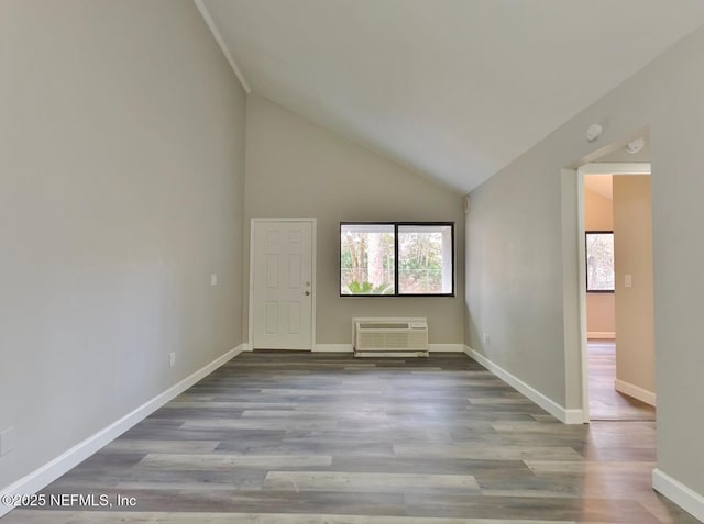 empty room with a wall unit AC, high vaulted ceiling, baseboards, and wood finished floors